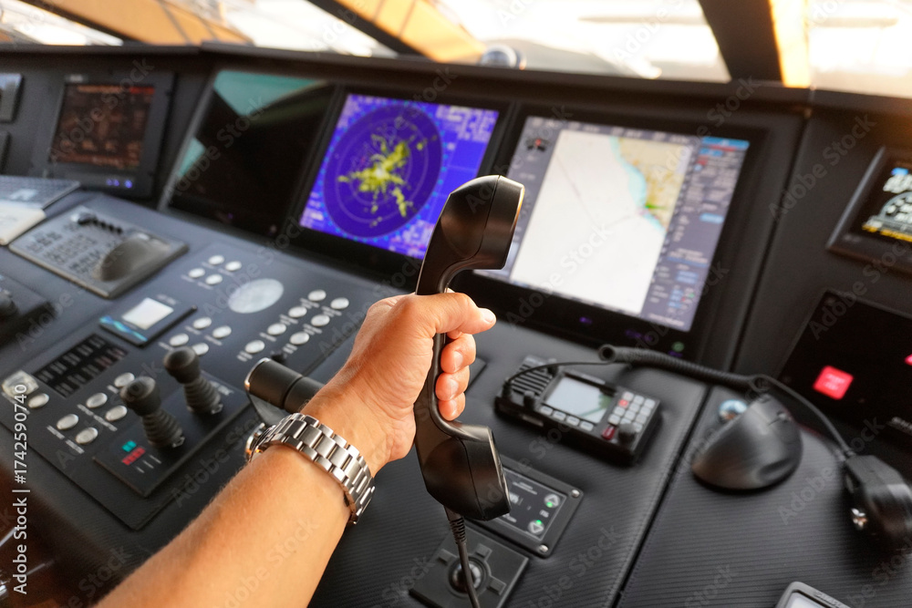 Captain holding a VHF radio handset in front of radar and chartplotter displays